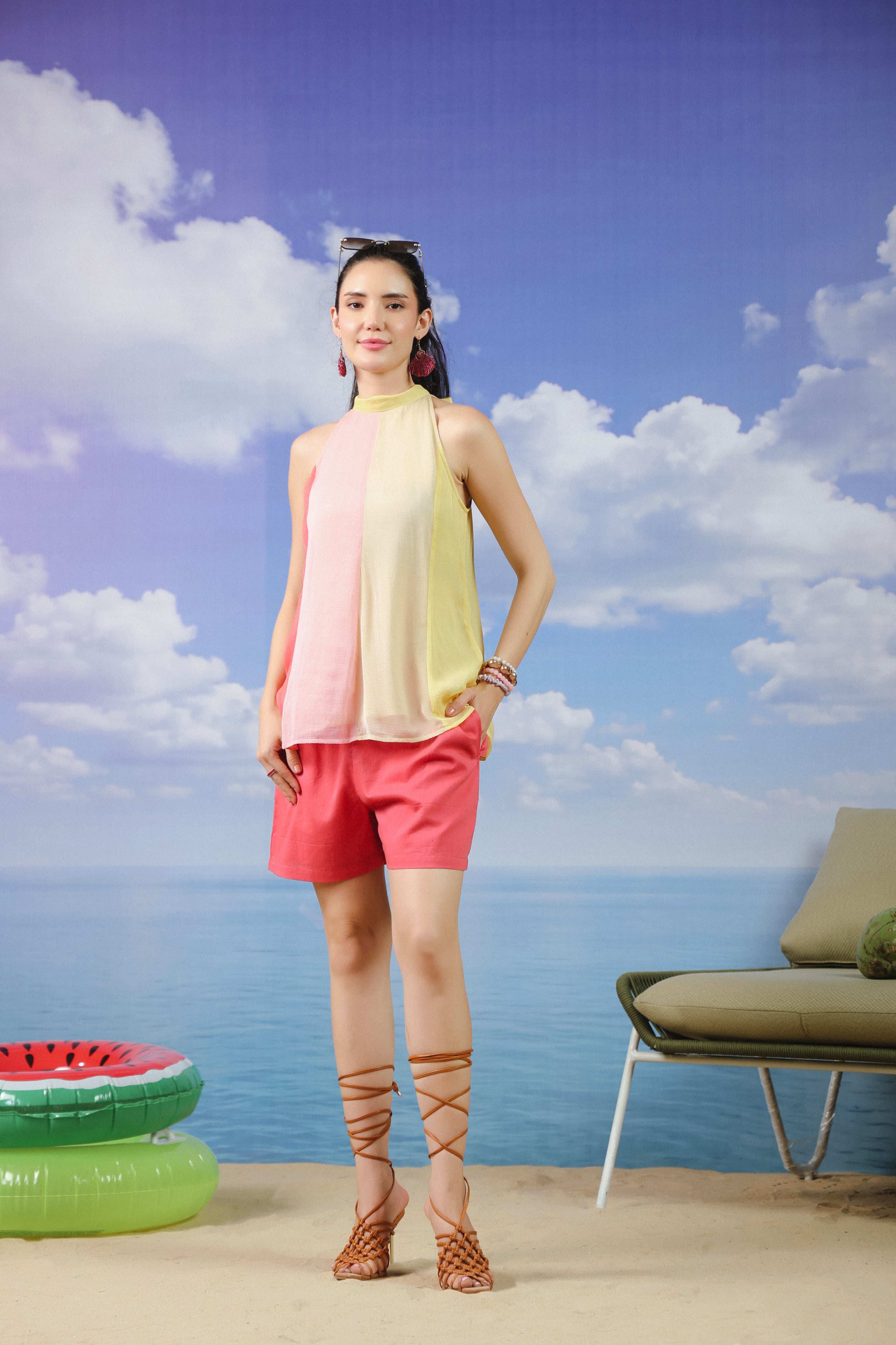 Woman wearing a pastel pink and yellow colorblock halter neck sleeveless top paired with coral pink shorts, creating a stylish summer co-ord outfit for beach vacations and casual wear.