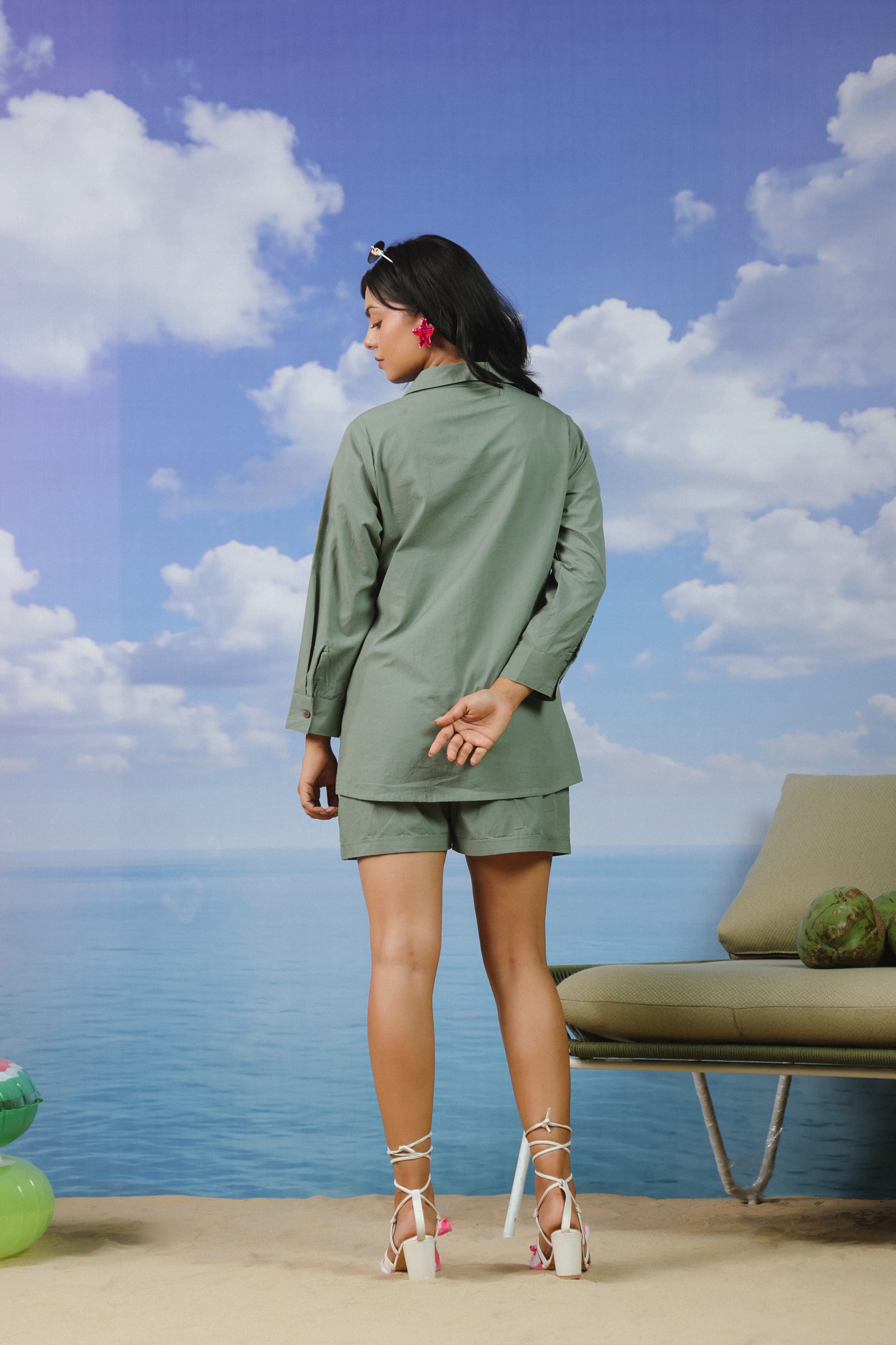 Woman wearing a sage green cotton shirt and shorts co-ord set featuring a classic button-down collared shirt with full sleeves and matching relaxed-fit shorts, ideal for casual outings, vacations, resort wear, and everyday summer styling.