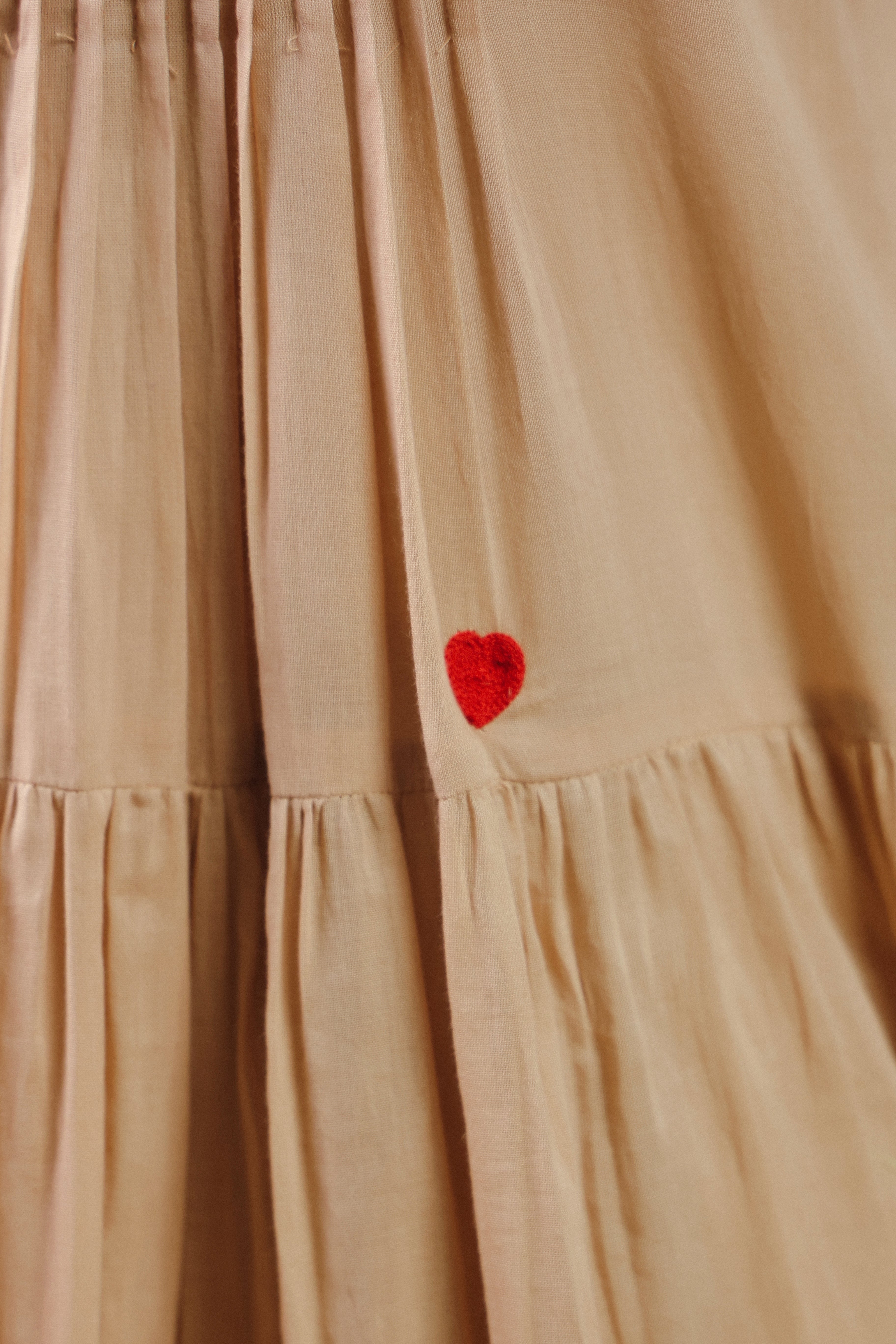 Woman wearing a beige sleeveless cotton midi dress with a high halter neckline, pleated bodice, and flowy tiered skirt, offering a chic and elegant look perfect for vacations, resort wear, beach outings, brunches, and summer occasions.