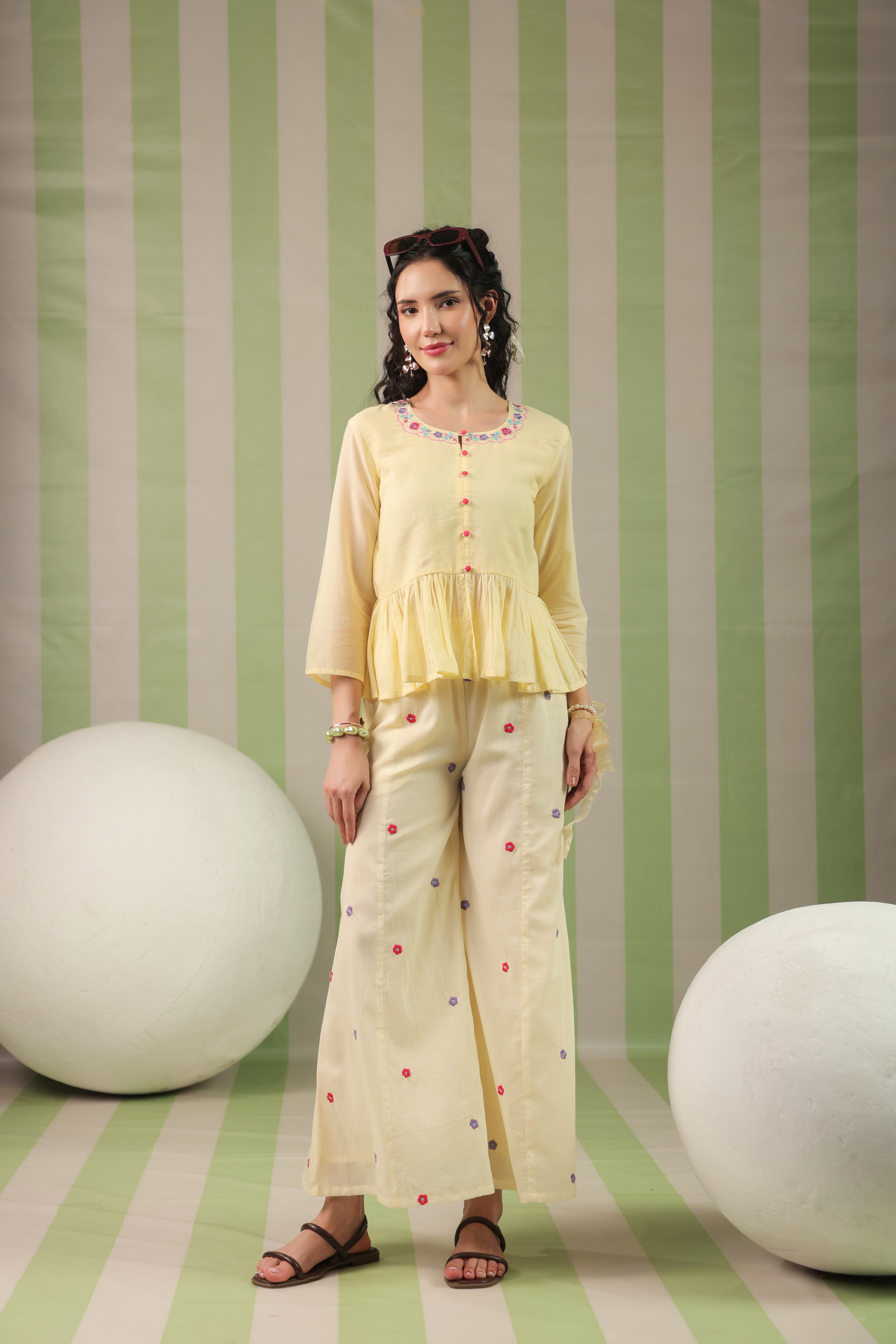 Woman wearing a blush yellow embroidered peplum co-ord set with wide-leg palazzo pants, featuring a floral embroidered neckline and relaxed elegant fit. Perfect for casual and festive occasions.