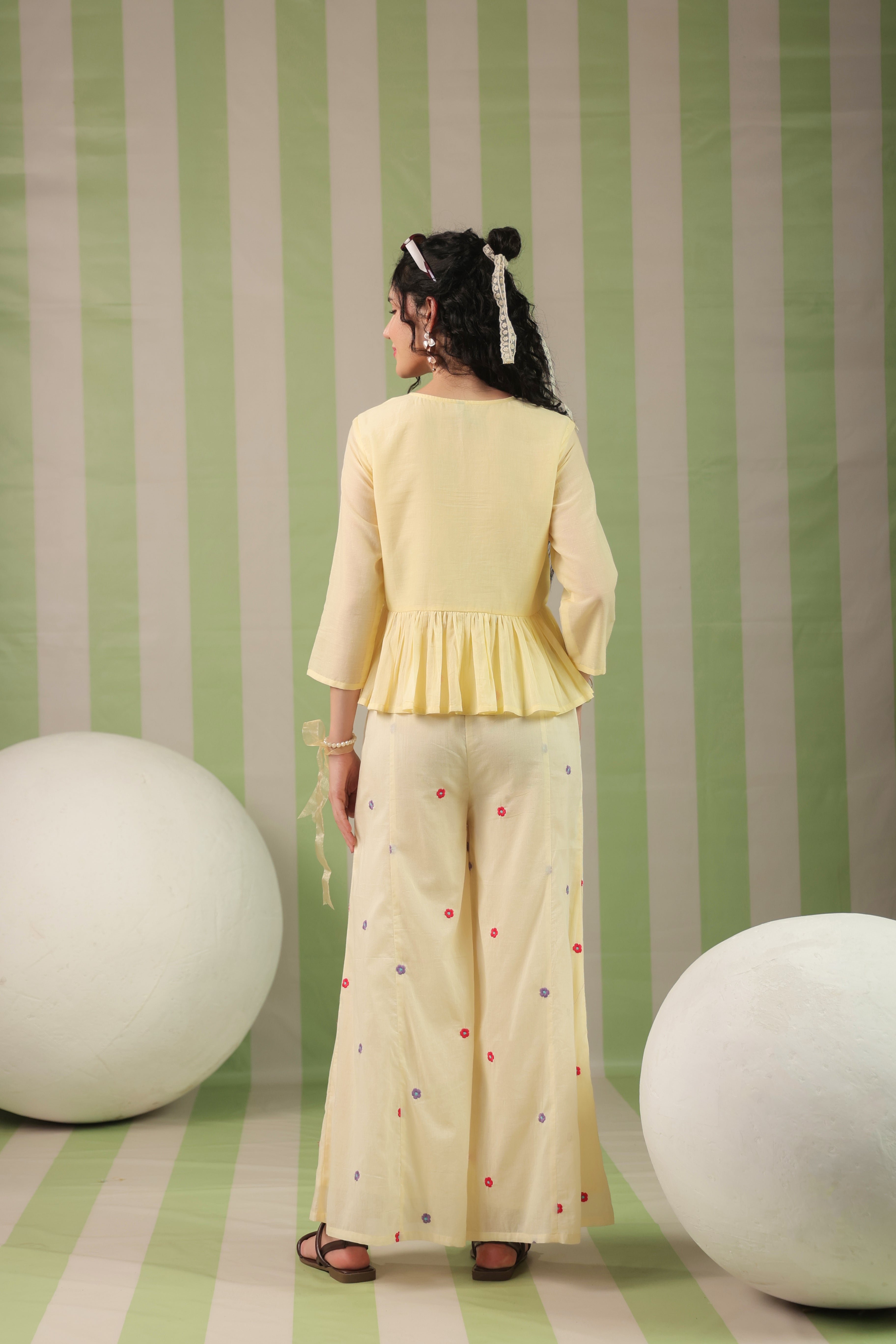 Woman wearing a blush yellow embroidered peplum co-ord set with wide-leg palazzo pants, featuring a floral embroidered neckline and relaxed elegant fit. Perfect for casual and festive occasions.