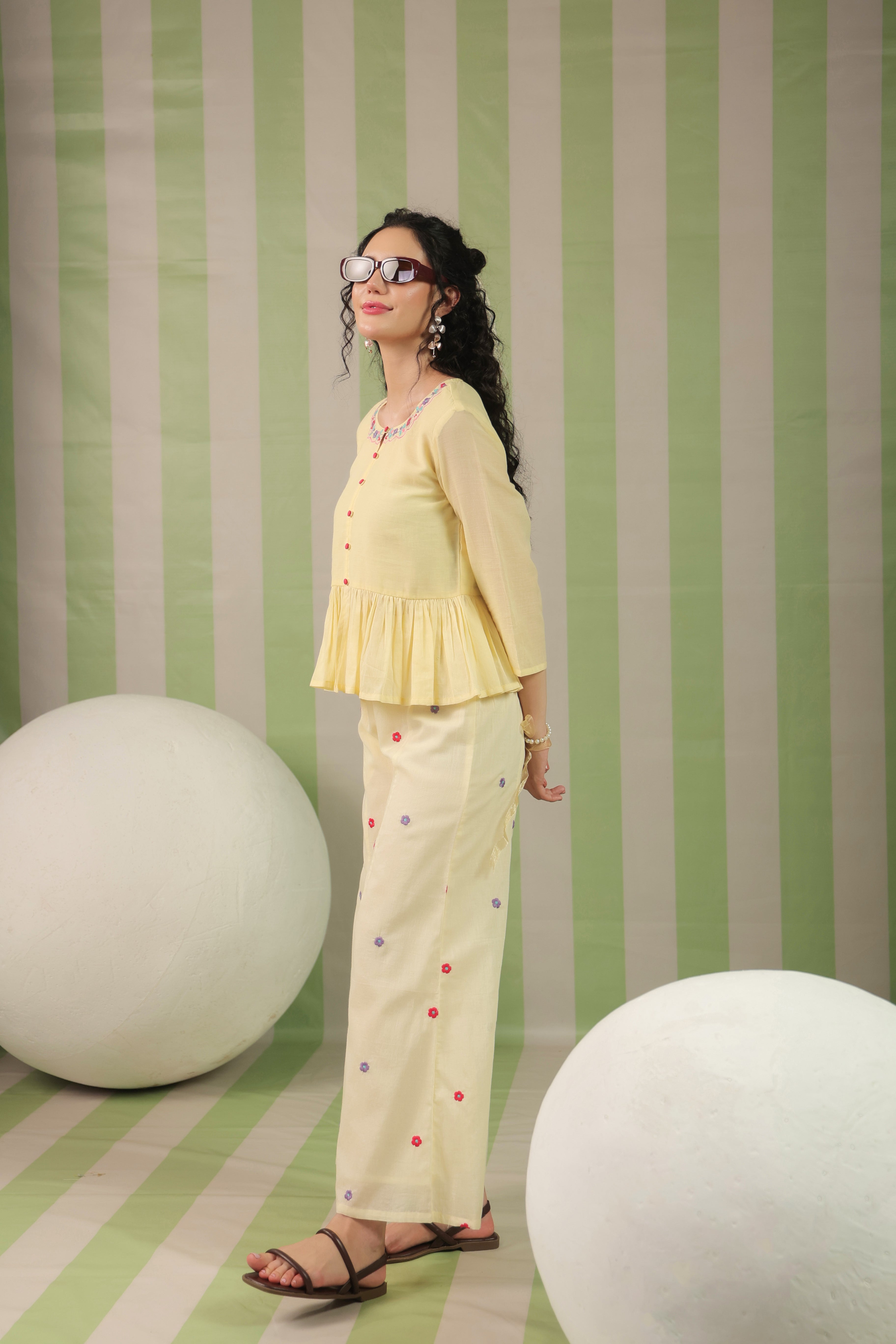 Woman wearing a blush yellow embroidered peplum co-ord set with wide-leg palazzo pants, featuring a floral embroidered neckline and relaxed elegant fit. Perfect for casual and festive occasions.