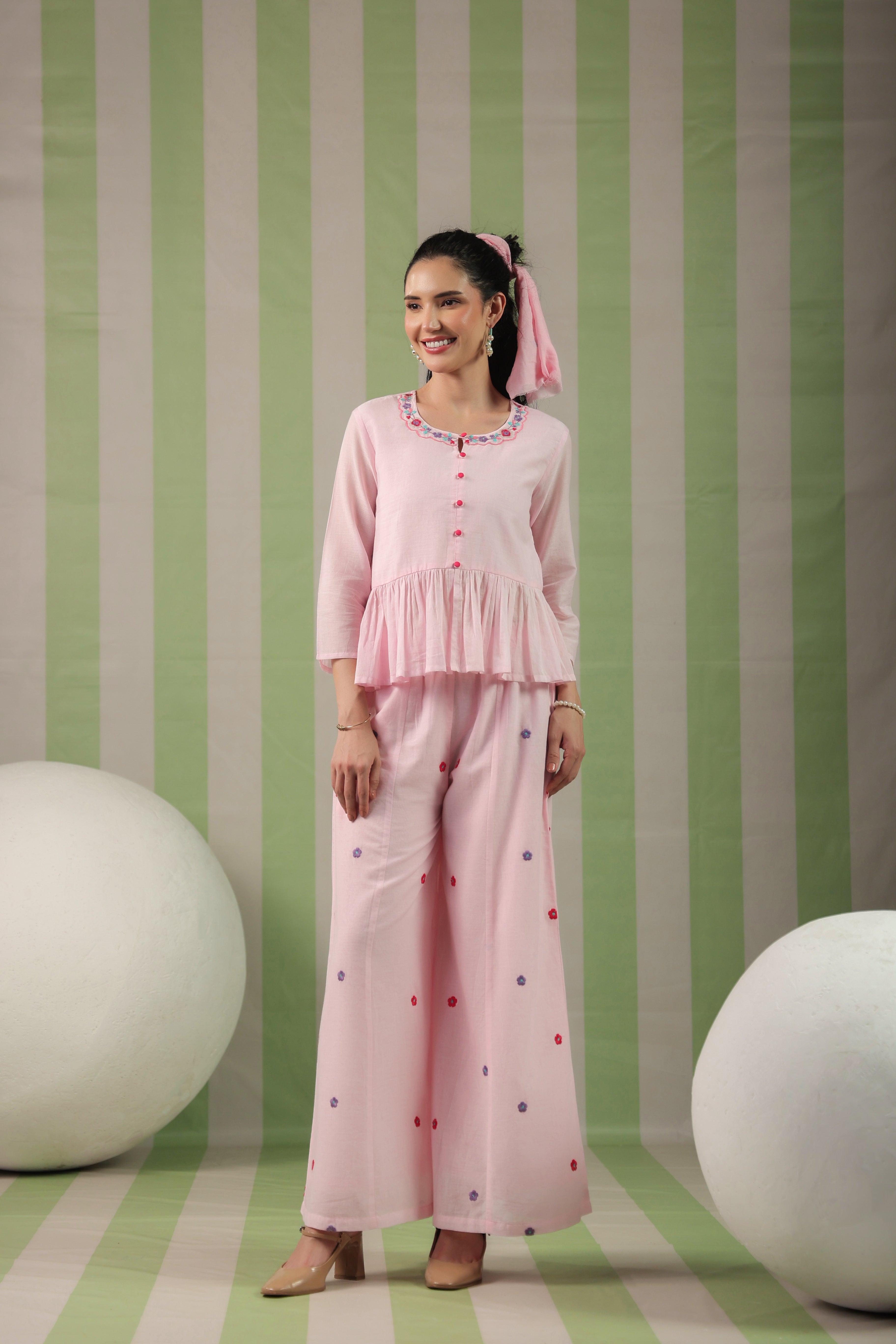 Woman wearing a blush pink  embroidered peplum co-ord set with wide-leg palazzo pants, featuring a floral embroidered neckline and relaxed elegant fit. Perfect for casual and festive occasions.