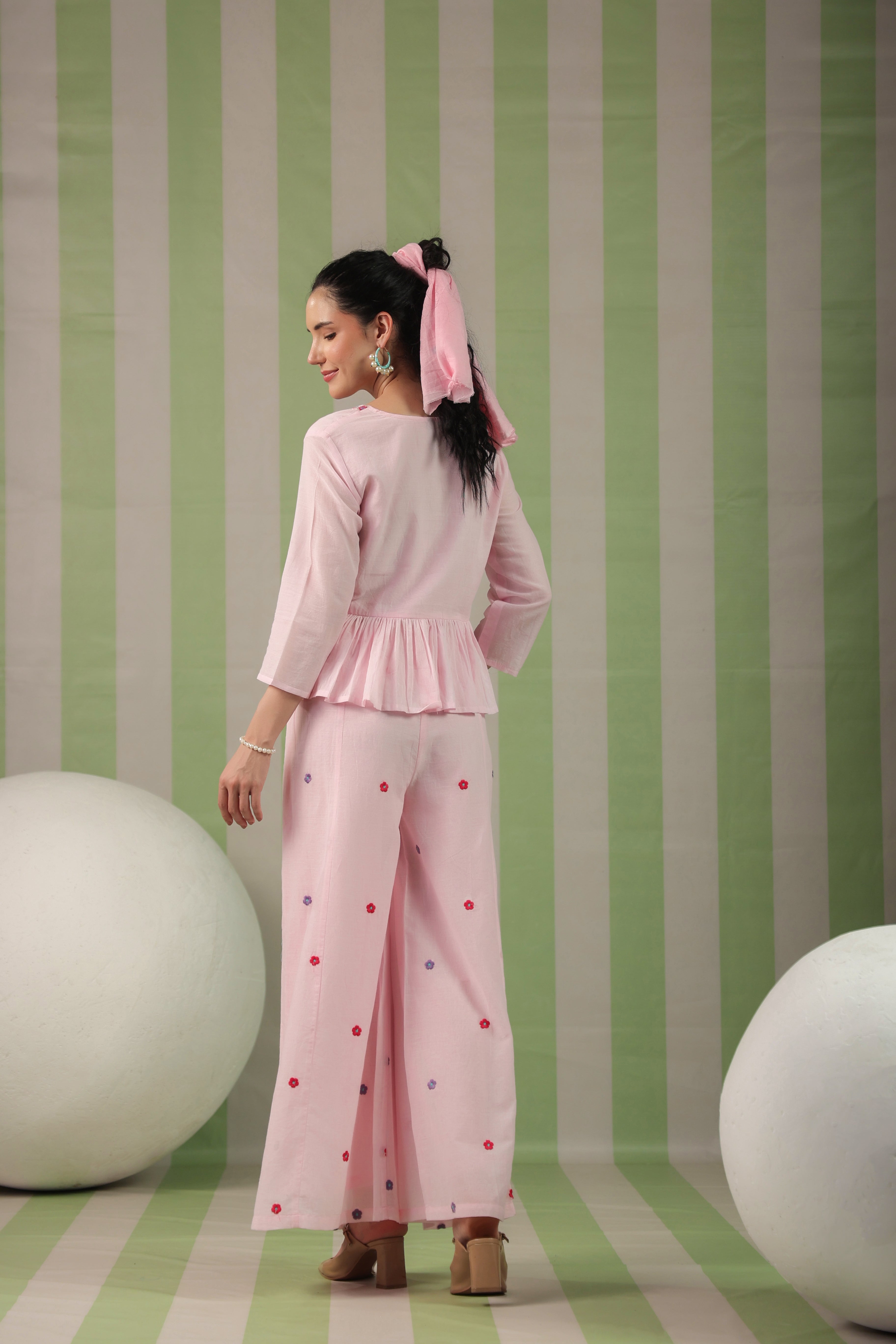 Woman in a pink outfit with polka dots standing against a striped green and white wall.