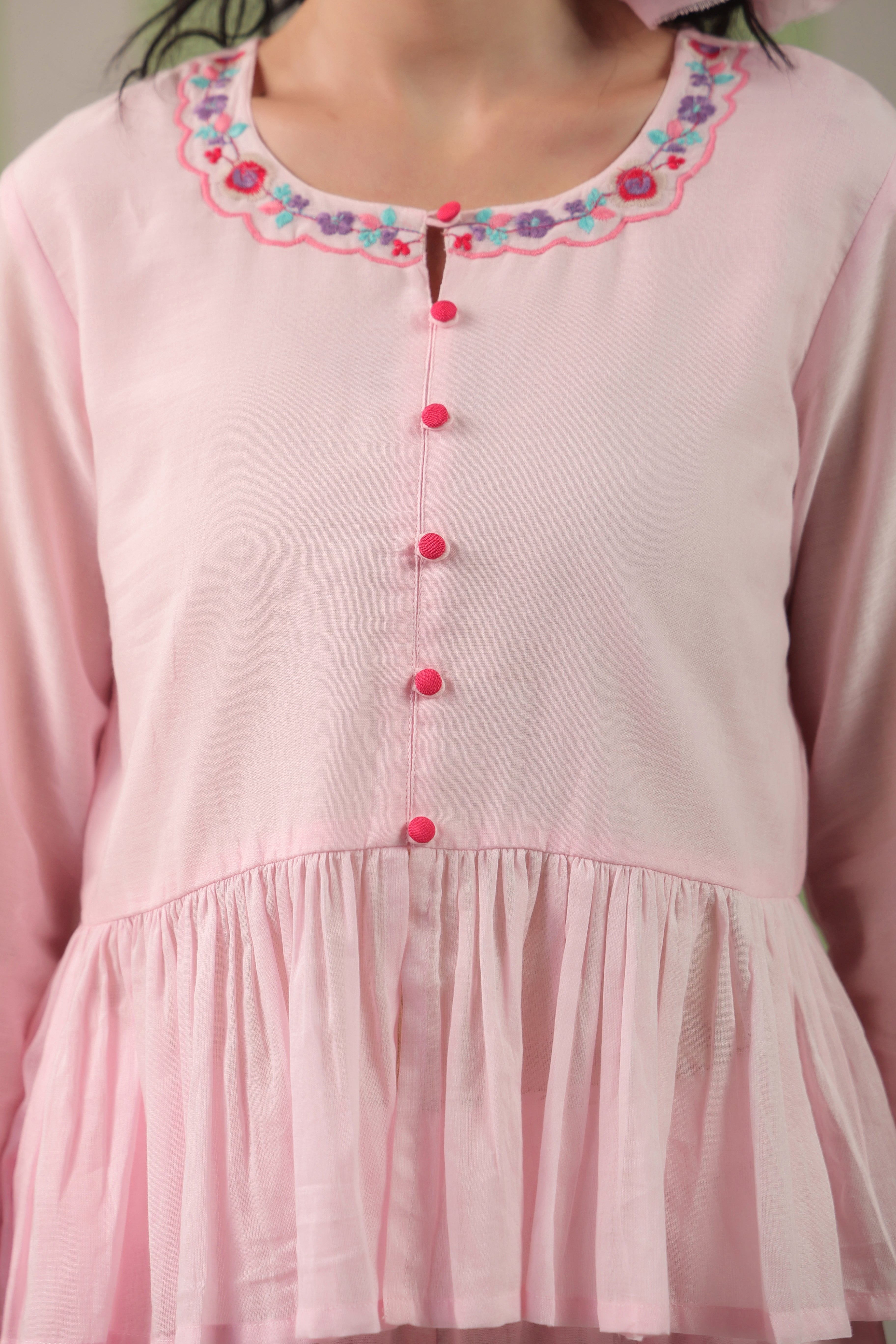 Woman wearing a blush pink  embroidered peplum co-ord set with wide-leg palazzo pants, featuring a floral embroidered neckline and relaxed elegant fit. Perfect for casual and festive occasions.