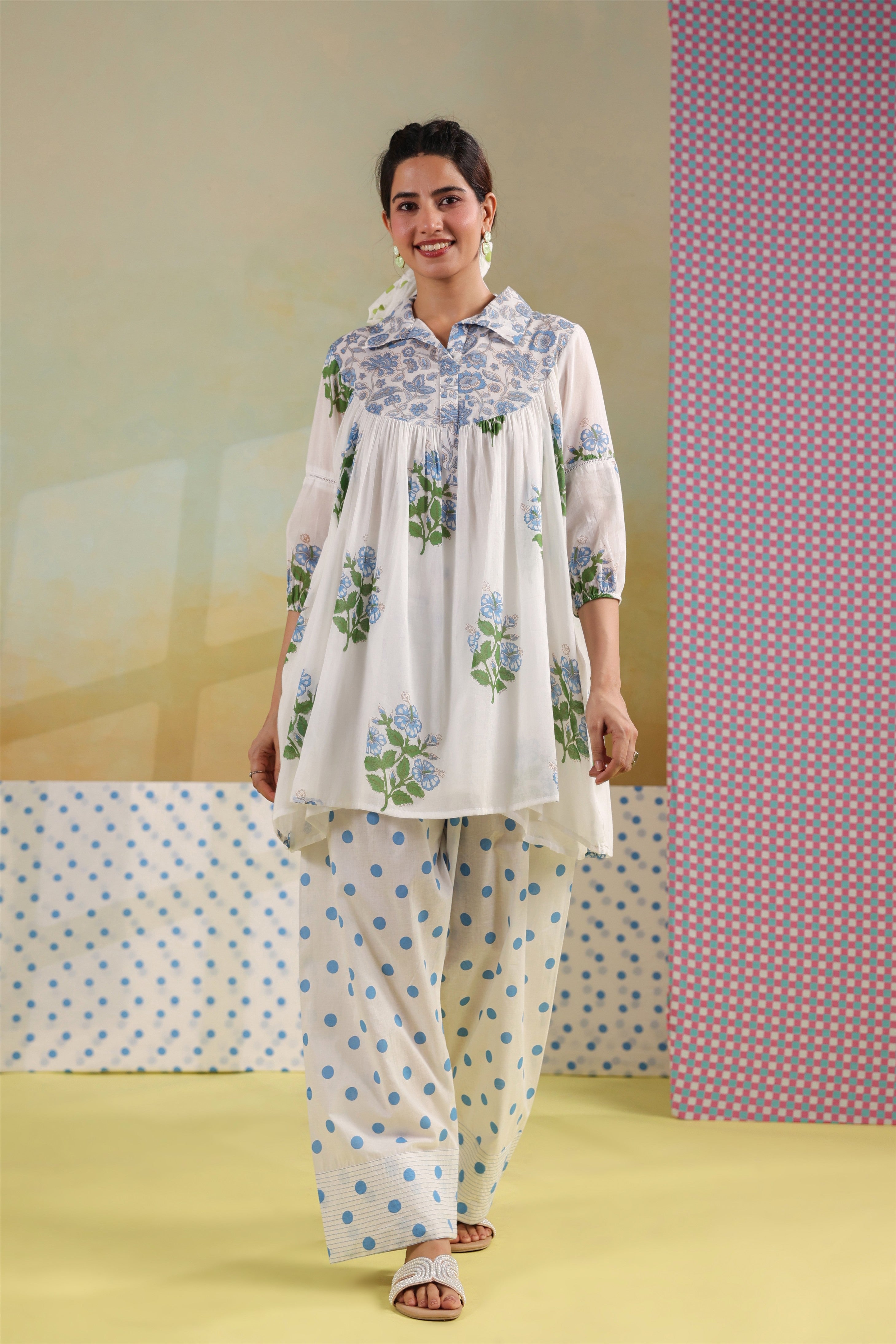 Woman wearing a white cotton gathered tunic with blue floral prints and a shirt collar, paired with blue polka dot straight pants, creating an elegant and comfortable co-ord set for casual, office, and summer wear.