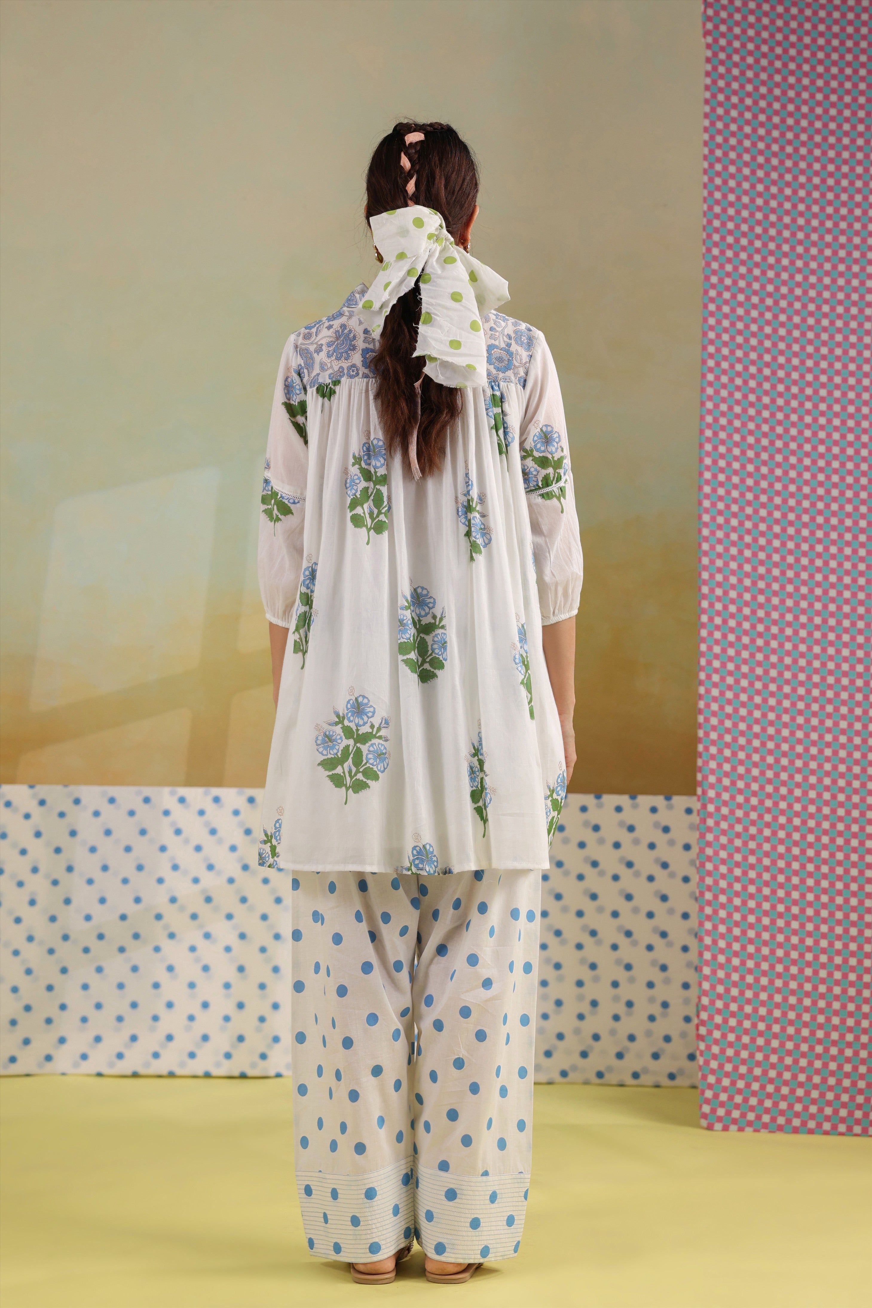 Woman wearing a white cotton gathered tunic with blue floral prints and a shirt collar, paired with blue polka dot straight pants, creating an elegant and comfortable co-ord set for casual, office, and summer wear.