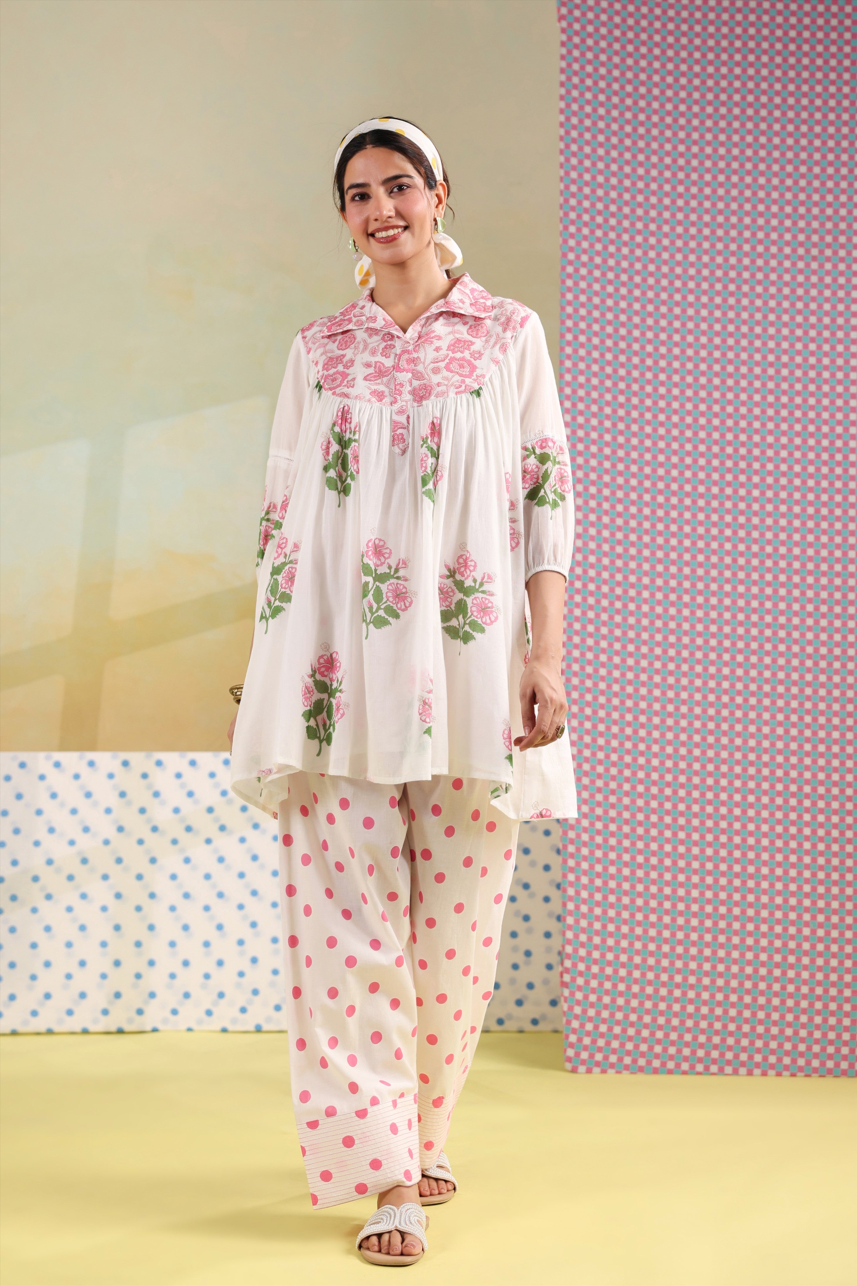 Woman wearing a white cotton floral printed gathered tunic with a shirt collar paired with pink polka dot straight pants, perfect for casual, office, and summer wear.
