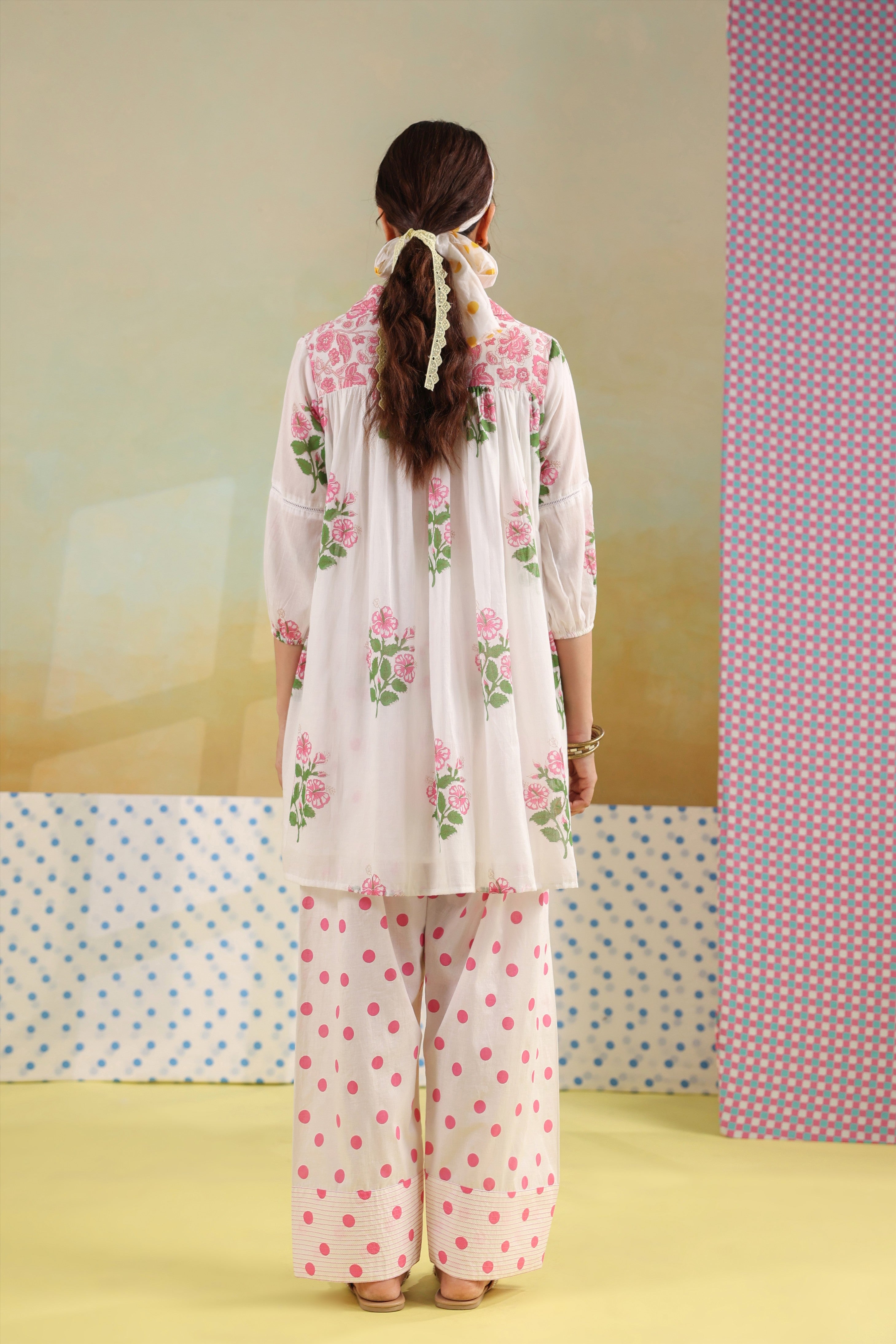 Woman wearing a white cotton floral printed gathered tunic with a shirt collar paired with pink polka dot straight pants, perfect for casual, office, and summer wear.