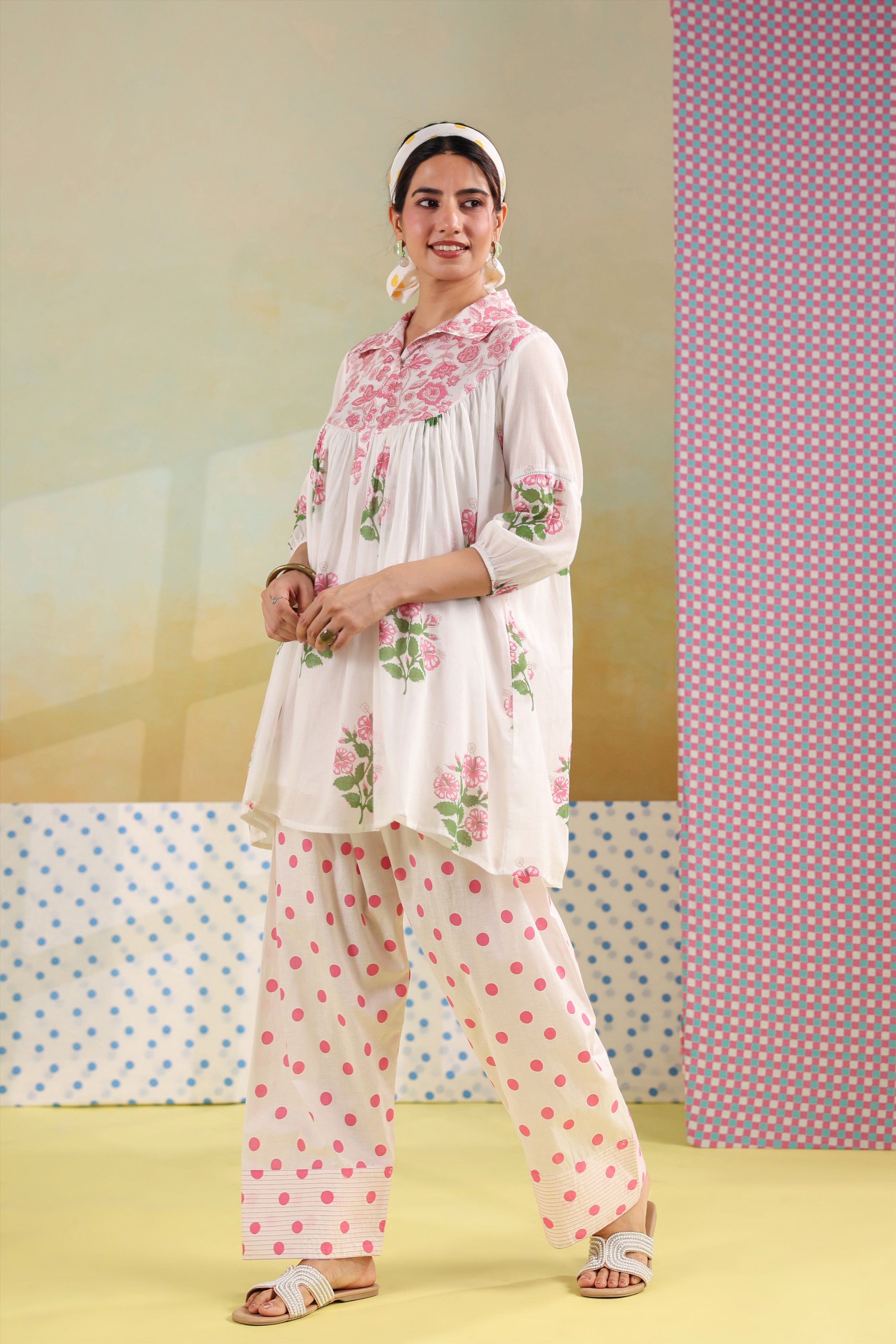 Woman wearing a white cotton floral printed gathered tunic with a shirt collar paired with pink polka dot straight pants, perfect for casual, office, and summer wear.