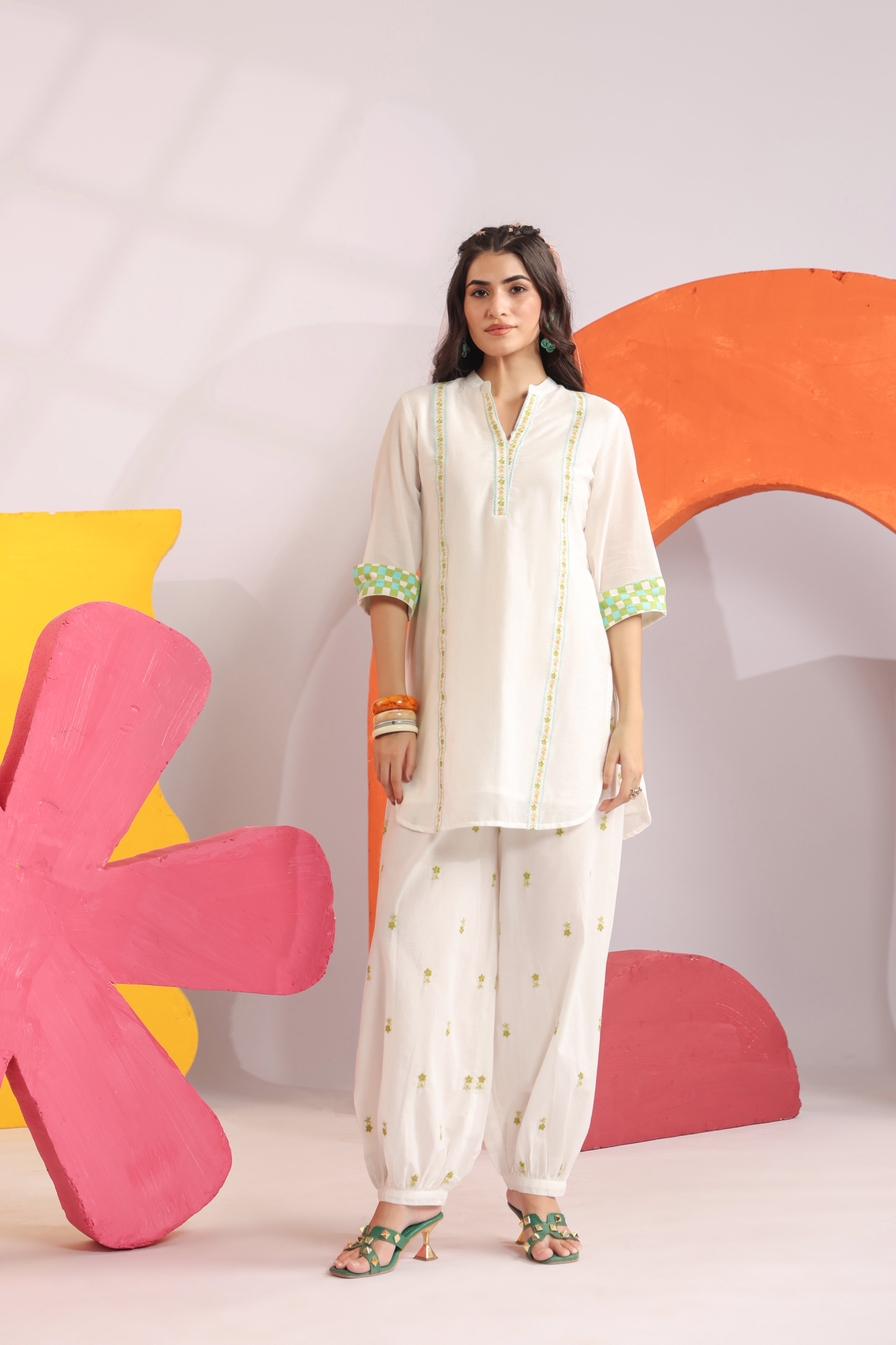 Woman wearing a white cotton embroidered straight-fit kurta with a Mandarin V-neck and contrast check sleeve cuffs, paired with white printed balloon pants, ideal for office wear, casual outings, and summer fashion.