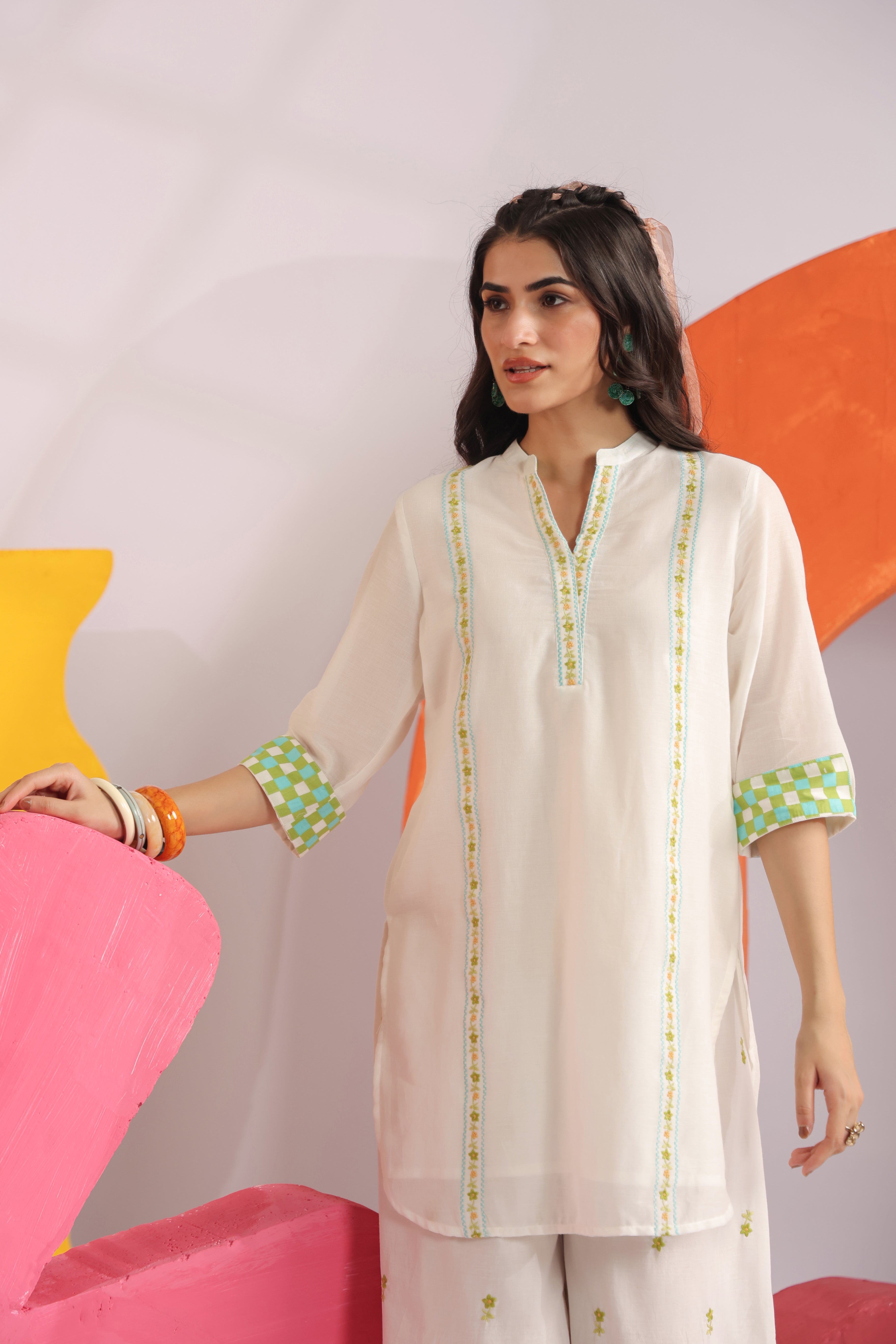 Woman wearing a white cotton embroidered straight-fit kurta with a Mandarin V-neck and contrast check sleeve cuffs, paired with white printed balloon pants, ideal for office wear, casual outings, and summer fashion.