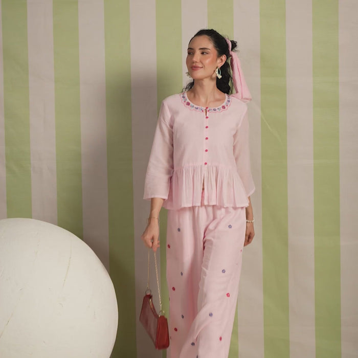 Woman wearing a blush pink  embroidered peplum co-ord set with wide-leg palazzo pants, featuring a floral embroidered neckline and relaxed elegant fit. Perfect for casual and festive occasions.