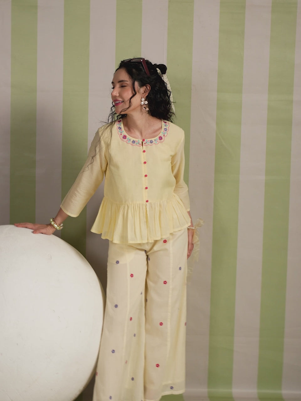 Woman wearing a blush yellow embroidered peplum co-ord set with wide-leg palazzo pants, featuring a floral embroidered neckline and relaxed elegant fit. Perfect for casual and festive occasions.